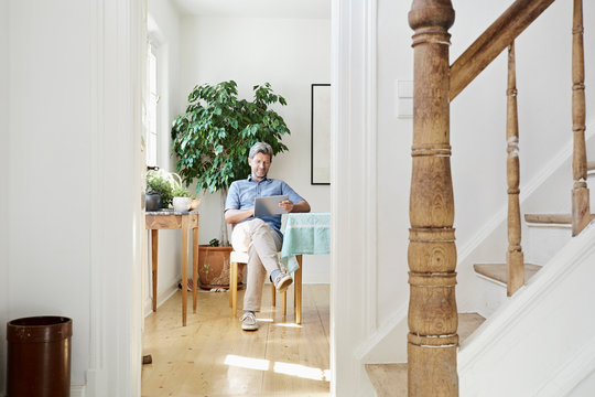Mature man sitting in his dining room, using tablet