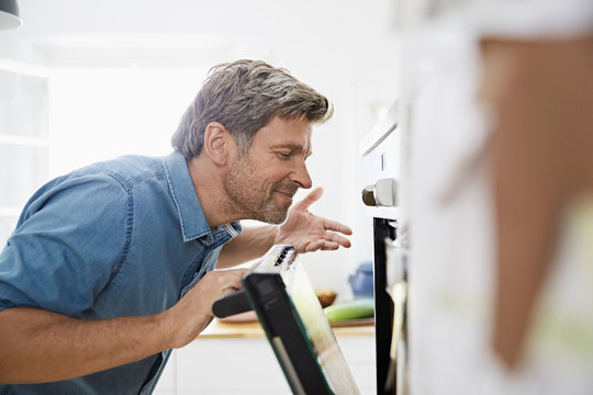 Mature man in his kitchen smelling meal in the oven