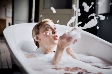 Blond woman taking bubble bath blowing foam in the air