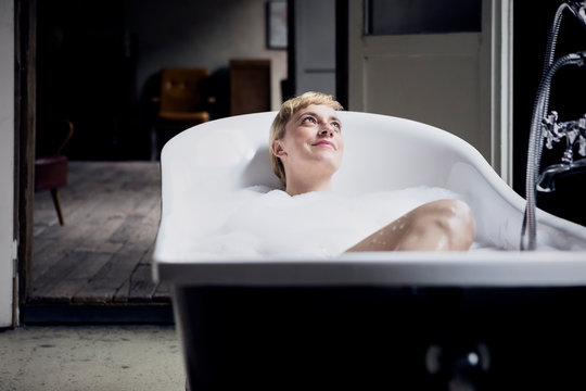 Portrait of happy woman taking bubble bath in a loft