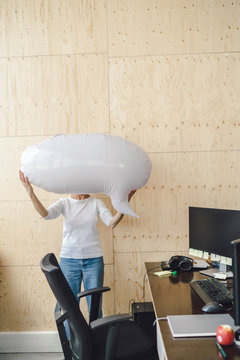 Woman standing in office, holding inflatable speech bubble in front of her face
