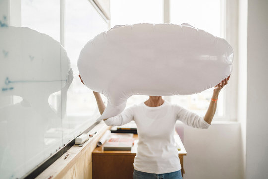 Woman standing in office, holding inflatable speech bubble in front of her face