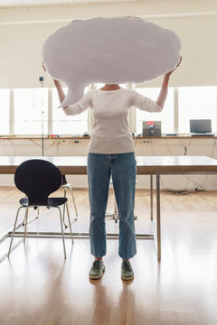 Woman standing in office, holding inflatable speech bubble in front of her face