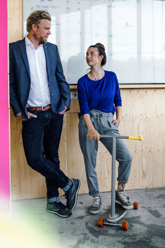 Mature man and his assistant with scooter, standing in office in front of white board