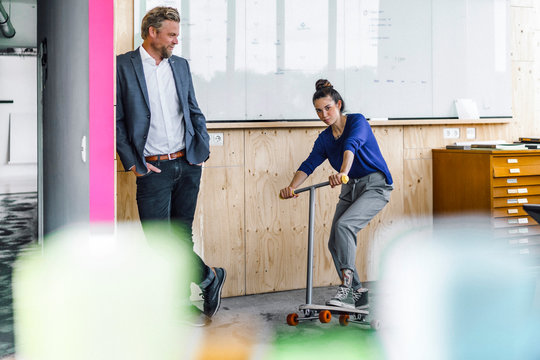 Mature man and his assistant playing with scooter, standing in office in front of white board