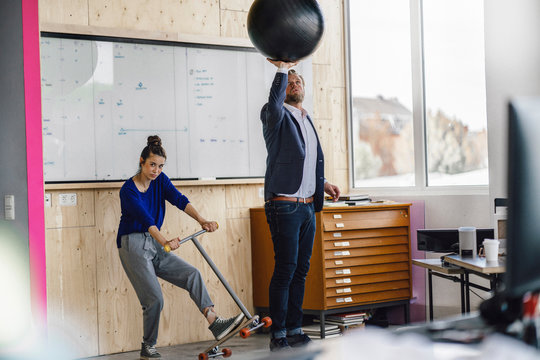 Mature man and his assistant playing with scooter, standing in office in front of white board