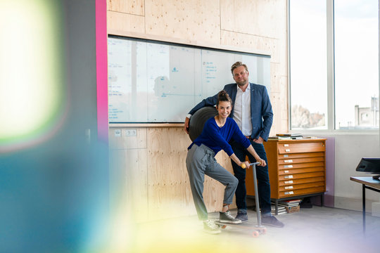 Mature man and his assistant with scooter, standing in office in front of white board