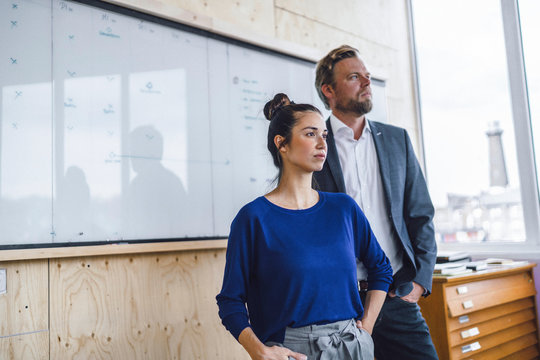 Mature man and his assistant, standing in office in front of white board