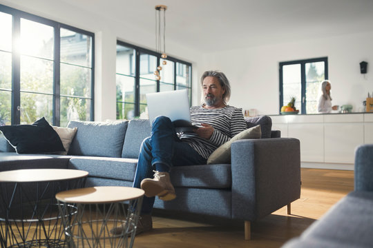 Senior man sitting on couch, using laptop