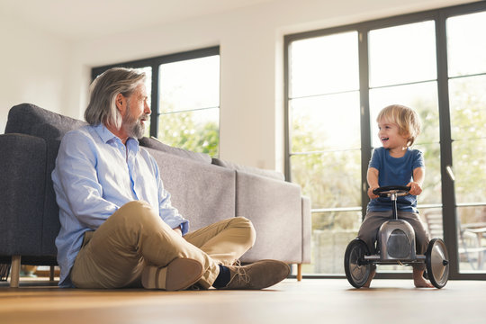 Grandfather playing with grandson, sitting on toy car