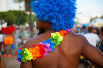 Close up of brightly colored rainbow flower lei and blue afro wig on an unrecognizable man at a...