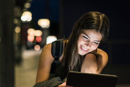Portrait of young woman with headphones and tablet waiting at station by night