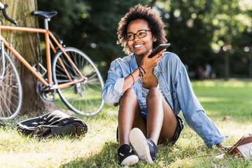 Smiling young woman resting in park with cell phone and tablet