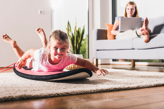 Little girl playing on surfboard in living room