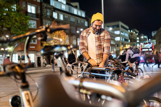UK, London, man unlocking his bike and commuting at night in the city