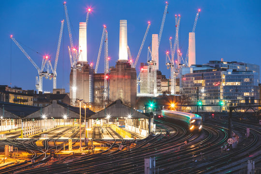 United Kingdom, England, London, view of rail tracks and trains in the evening, former Battersea Power Station and cranes in the background
