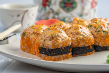 Baked rolls with scallop , spicy sauce, cream cheese and mango with rice on white plate with gold border. Asian menu