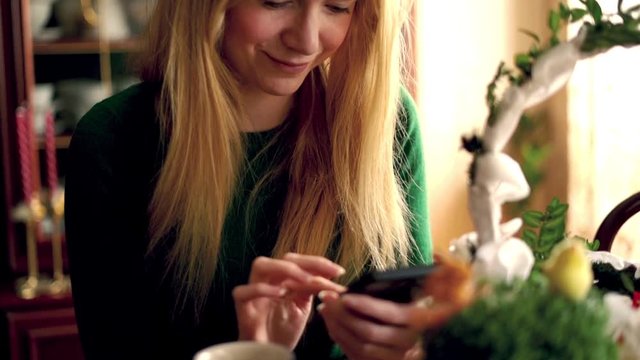 Beautiful woman exchanged easter greetings on smartphone sitting close to easter basket, super slow motion