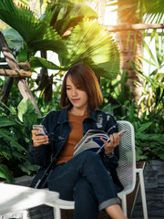Young teen beautiful woman reading book and listening to music in relaxing manner in the coffee cafe. Female student reads book in free time in outdoors cafe. 
