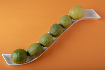 Limes arranged on a white porcelain tray over orange background with negative space for text ideal for food and fruit signs and grocery business