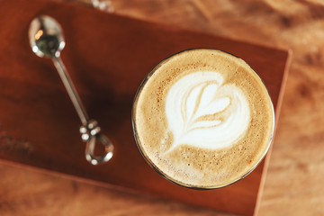 cups of cappuccino with latte art and spoon on wooden background