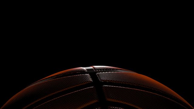 basketball with back lighting slowly spins at bottom of frame over black - 3d.