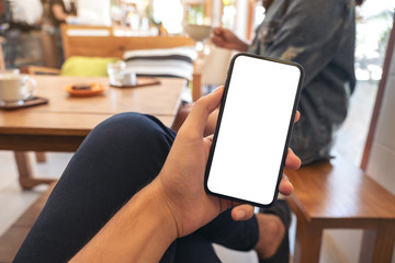 Mockup image of a man's hand holding black mobile phone with blank white screen with woman sitting in cafe