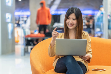 Asian woman using credit card with mobile phone for online shopping in department store over the clothes shop store background, technology money wallet and online payment concept, credit card mockup