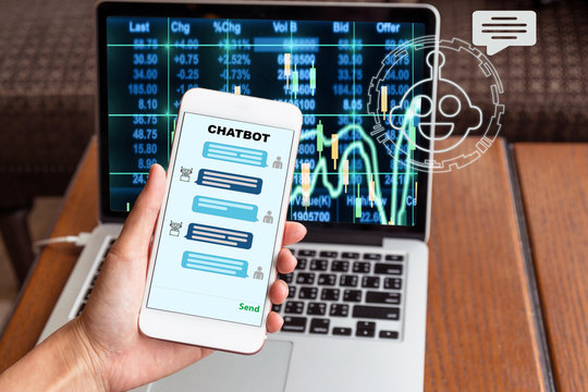 Female hand holding mobile phone showing the chatbot message While being decided place the order over the Stock market chart over the computer laptop screen, Business investment with AI concept