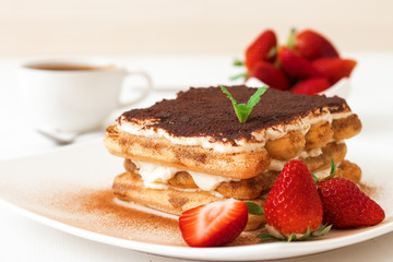 Tiramisu, homemade sweet cheesecake style dessert, on white plate embellished with fresh mint and a...