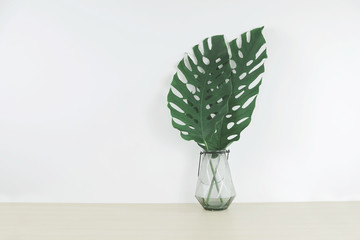 Tropical leaves in a glass vase on wood table, front view, space for a text.