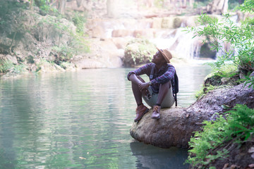 African man traveler sittng at water fall nature with hands up. Freedom concept