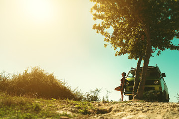 Young female traveler leaned against her old timer van while enjoying on a warm sunny summer day - Image
