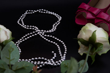 8th of march, woman`s day, pinkcolor high-heels, silver beads, 8 number, black background, three white roses