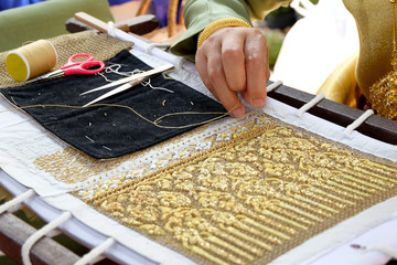 Women working on gold silk thread by hand embroidering on white canvas
