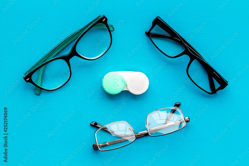 Wall mural eye problems. glasses with transparent lenses and contact lenses on blue background top view