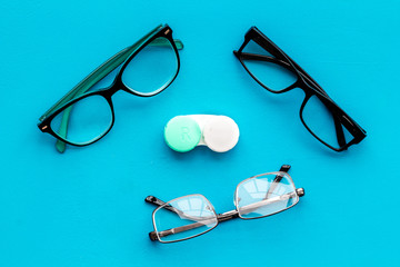 Eye problems. Glasses with transparent lenses and contact lenses on blue background top view
