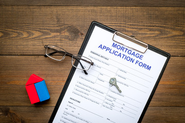 Mortgage concept. Mortgage application form near key and house made of constructor on dark wooden background top view copy space