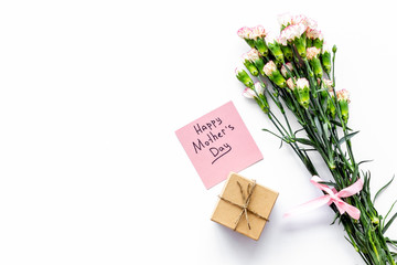 Mother's Day congratulations. Carnations and gift box on white background top view copy space
