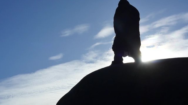 man in hoodie pissing on the edge of rock back view silhouette