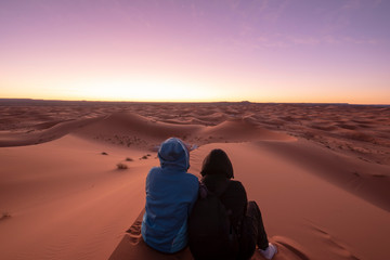 Fototapeta na wymiar Night landscape with loving couple, boy and girl sitting on the sand dunes looking the horizon . Sunrise in the desert Sahara, Merzouga , Morocco . man and woman . Concept of love