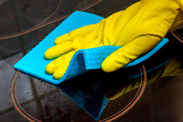 washing the electric stove with a glass-ceramic surface - a gloved hand with a rag close-up