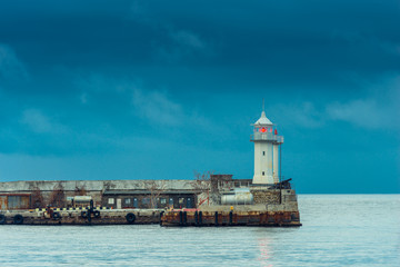 Fototapeta na wymiar Horizontal photo of a lighthouse with a red lantern on the background of the sea and rainy blue clouds