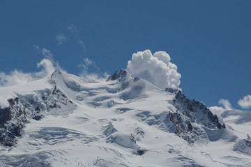 Fototapeta na wymiar snowy summit of Dufourspitze mountain with cumulus cloud, blue sky