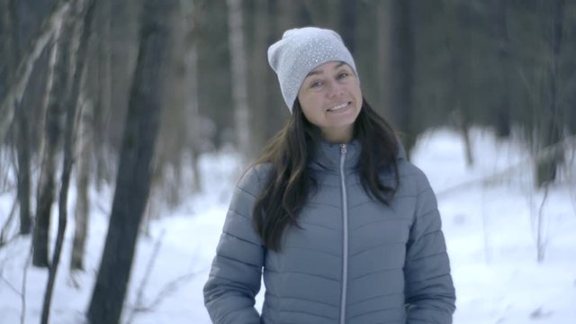 middle aged cheerful brunette woman is standing alone in snowy forest in winter day