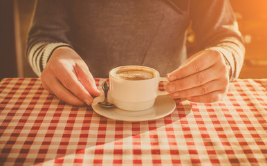 A man drinks cappuccino coffee at a cafe table.