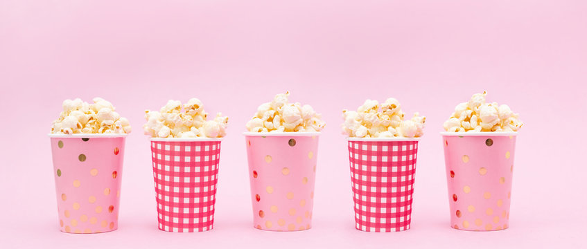 several cups of popcorn on a pink background