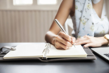 Closeup of woman's hand writing on notebook. Freelance journalist working at home.