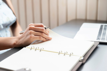 Closeup of woman's hand holding a pen on notebook. Freelance journalist working at home.