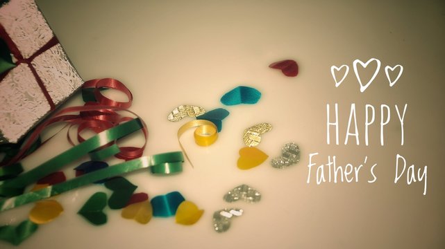 Happy Fatther's Day words with Colourful heart shape ribbon and small gift boxes on colorful bokeh, flare background. Image noise and light leaks.